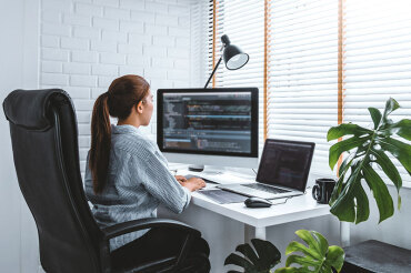 Woman in home office with large computer monitor and laptop