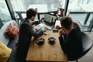 2 young businessmen looking at a laptop in a cafe