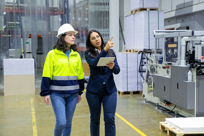 Manager walking through manufacturing factory with a worker and a tablet